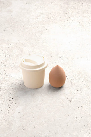 Small white container with a lid next to a brown egg on a light gray surface