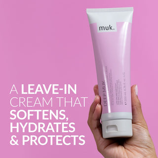 Hand holding a tube of muk leave-in cream against a pink background