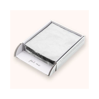 A stack of textured white paper napkins inside an open white cardboard box with a hinged flap, set against a solid pale pink background.