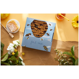 Product packaging with honeycomb design on a table with flowers and honey.