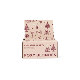A display box of pre-cut pop-up foil in the shade 'Foxy Blondes' against a plain white background. The box is light pink with dark red illustrations of Christmas trees, gifts, and martini glasses.