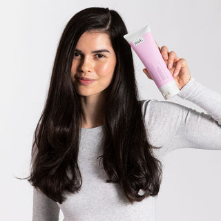 Woman holding a pink and white hair care product against a light background