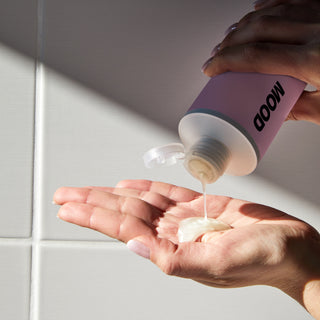 A bottle of MOOD Color Protect Shampoo with pink labelling in a shower setting advertising