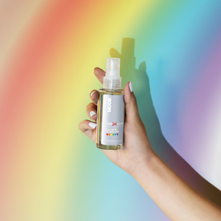 A clear spray bottle labeled 'MOOD Elixir Love Edition' with a rainbow-coloured stripe design, indicating a connection to LGBTQ+ community with a rainbow backgroud.