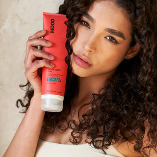 Woman holding a red tube of hair product with a neutral background