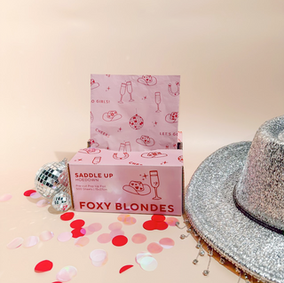 Foxy Blondes product box with a silver glittery hat and confetti on a beige background