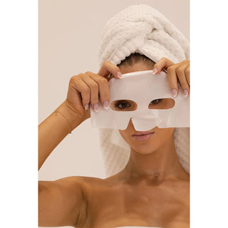 Woman wearing a white face mask with a towel on her head against a beige background