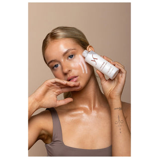 Woman applying a skincare product to her face with a beige background